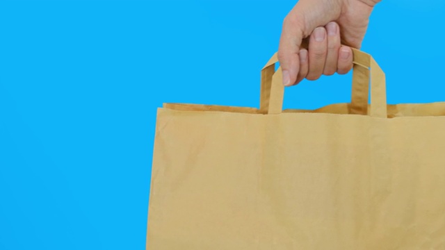 一个手持纸质购物袋，以蓝色为背景，使用可回收袋进行购物，拯救自然，保护环境视频下载