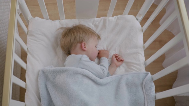 白天，可爱的小婴儿躺在柔软舒适的枕头上，上面盖着毯子，睡得很香视频素材