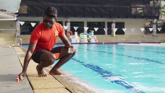 亚洲印度救生员游泳池测试套件正在游泳池中使用的水氯水平视频下载