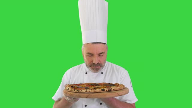 微笑的厨师闻着美味的披萨，在绿屏上做真正的果酱手势视频下载