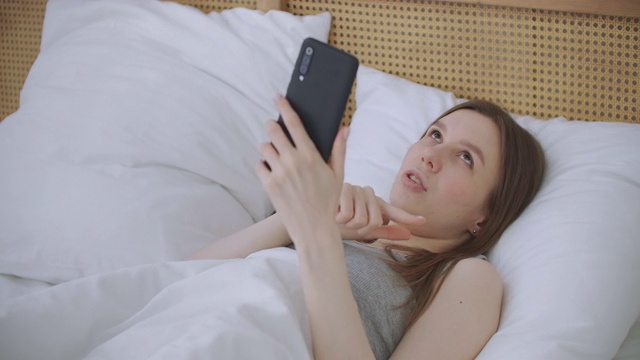 肖像妇女在家中用智能手机进行视频通话，在手机屏幕上向人们挥手。使用会议在线应用程序，保持社交距离视频素材
