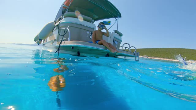 小男孩戴着潜水面罩从船上跳进蓝色的大海视频素材