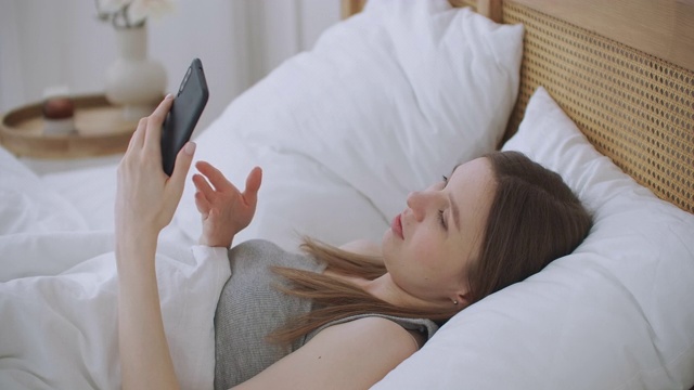 肖像妇女在家中用智能手机进行视频通话，在手机屏幕上向人们挥手。使用会议在线应用程序，保持社交距离视频素材
