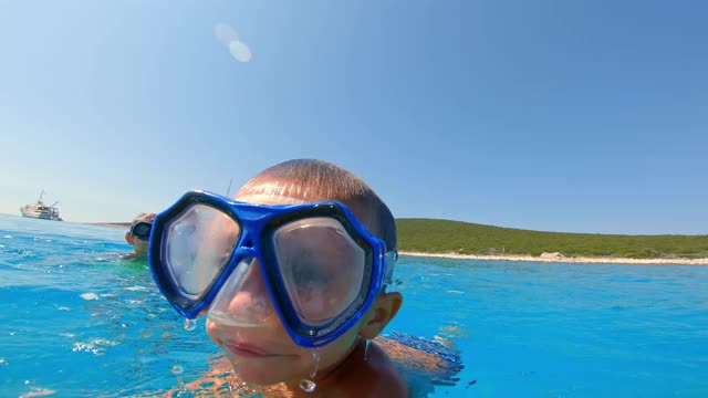小男孩戴着潜水面罩潜入水中，看着摄像机视频素材