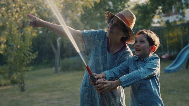 小男孩和奶奶笑着玩花园水管视频素材