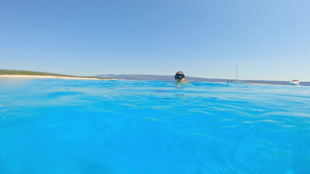 男孩戴着潜水面具，在一个阳光明媚的日子里在蓝色的大海里游泳视频素材
