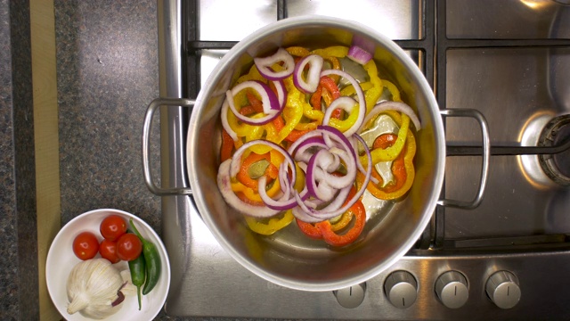厨房铁架上的辣椒和洋葱在平底锅里加热。视频素材