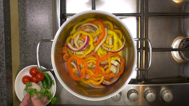 厨房铁架与香菜被添加到蔬菜煮在平底锅的俯视视图。视频素材
