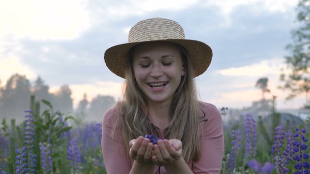 戴着帽子的女人吹起了紫色的卢平花的花瓣视频下载