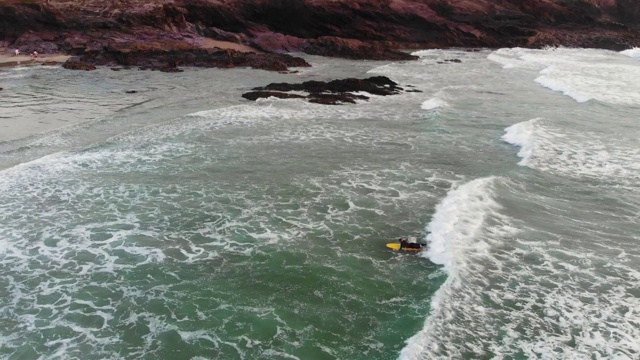 一位金发碧眼的新手女性冲浪者抓住了她的第一个波浪，并第一次站起来。在英国一个阴沉的春日，她身后的海岸布满了悬崖峭壁视频素材