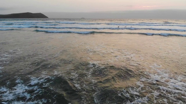 一个女冲浪女孩身体冲浪一个明亮的黄色冲浪板到海岸后，在一个柔和的色调的海洋。夕阳将天空沐浴在金色和粉红色的色调中视频下载