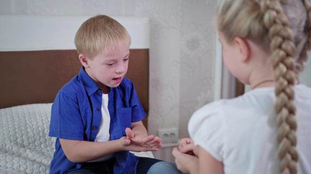 家庭娱乐，有唐氏综合症的小男孩和女孩坐在房间的床上玩石头剪刀布视频下载