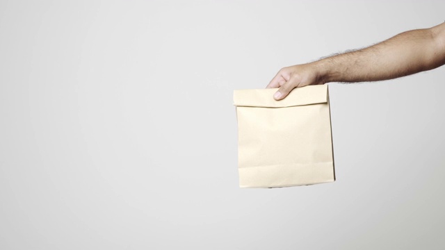 近手送餐员送食品纸袋在孤立的白色背景。物流货物网上购物概念。4 k决议。视频下载