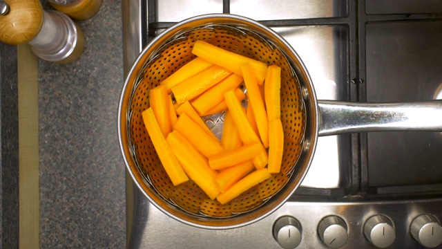 健康饮食。胡萝卜在厨房煤气灶上的炖锅里冒着热气。视频下载