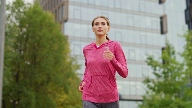 中等镜头的运动年轻女子在城市街道上跑步在日常慢跑锻炼视频下载