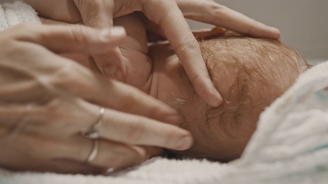一个小婴儿躺在床上，他的妈妈在他的脖子上涂霜视频素材