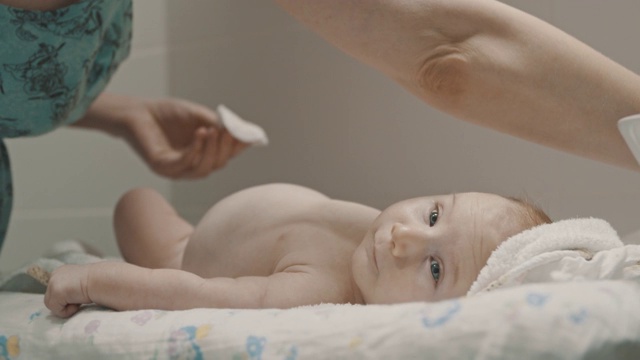 一个小婴儿躺在床上，他的妈妈在他的腿上涂药膏视频下载