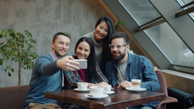 一群朋友在咖啡馆里自拍，摆着滑稽的姿势和手势拍着智能手机的相机视频下载