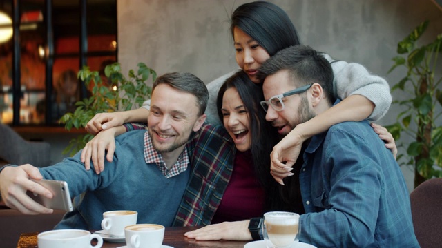 快乐的朋友们在咖啡馆自拍，用智能手机拍照，开心地拥抱和大笑视频下载
