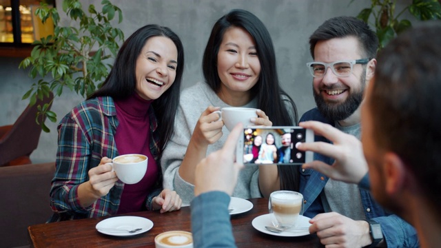 快乐的人们在咖啡馆碰杯庆祝，而一名男子正在用智能手机拍照视频下载