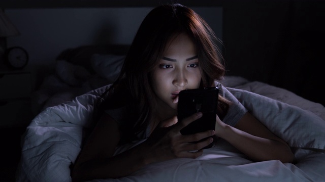 年轻的亚洲女性晚上在床上用智能手机。视频素材