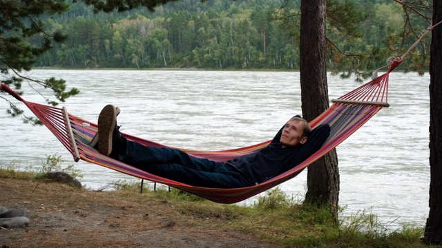 一个年轻人在河边的吊床上休息视频素材