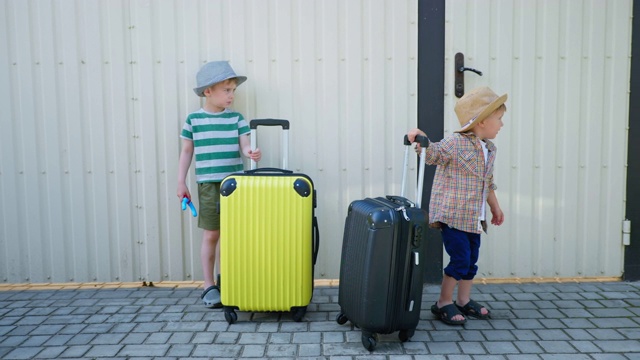为孩子们旅行，小可爱的男孩们戴着太阳帽，在白色栅栏的背景下，在手提箱附近玩得很开心视频下载