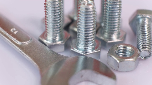 旋转组的镀锌金属螺丝，扳手和螺母关闭。不锈钢螺栓隔离在白色背景上。视频素材