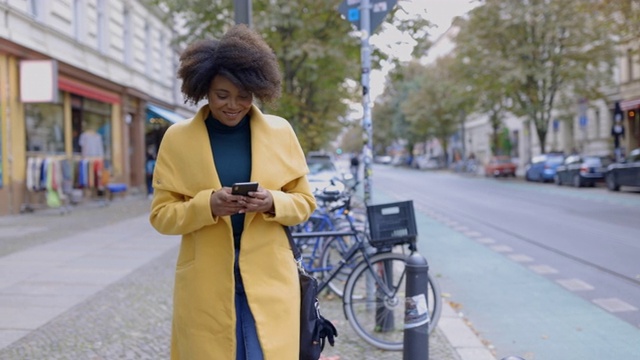 穿着夹克的女人在人行道上用智能手机视频下载