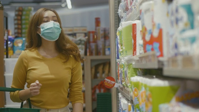 年轻女性戴着口罩在超市购物。视频下载