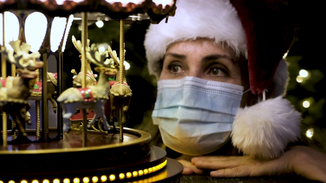 成熟的女人戴着圣诞老人的帽子看着玩具旋转木马视频下载