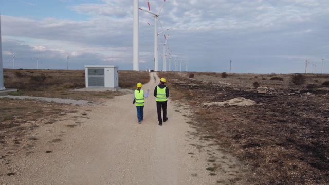 可再生能源系统。鸟瞰图电力维护工程师工作在附近的风力涡轮机发电站与阴沉的天空在他们身后。两位工程师同事的商务会议。团队合作。视频素材