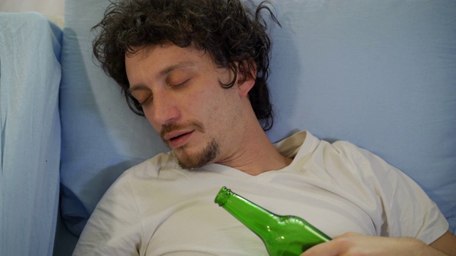 一个男人手里拿着一瓶啤酒睡觉——酗酒的概念视频下载