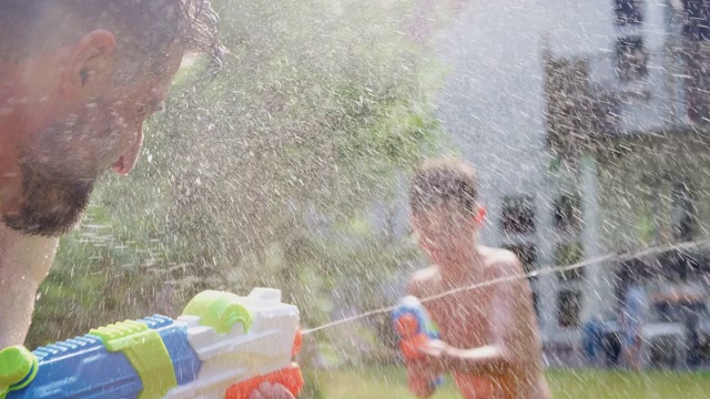 穿着游泳衣的一家人在夏日花园用水枪打水仗视频素材