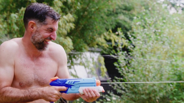 穿着游泳衣的一家人在夏日花园用水枪打水仗视频素材