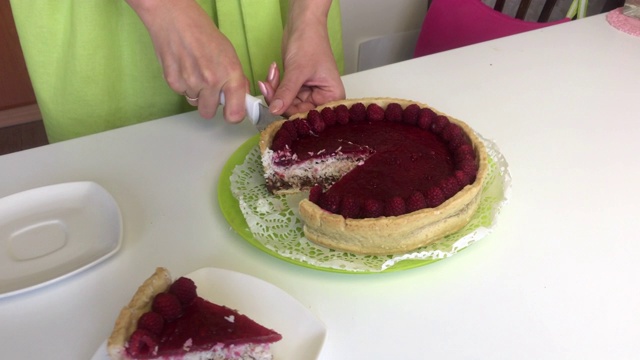 一个女人用覆盆子果冻切莱文顿蛋糕。她把它放在一个碟子上。点缀以树莓。视频素材