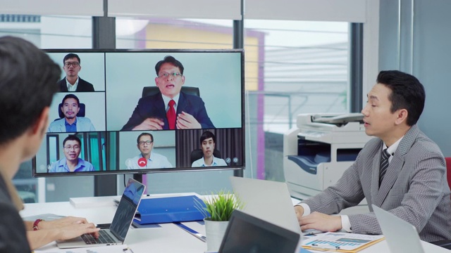 一群商务人士在董事会会议室与一位同事进行视频通话。视频素材