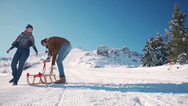 微笑的年轻夫妇在雪橇上一起滑下雪山视频素材