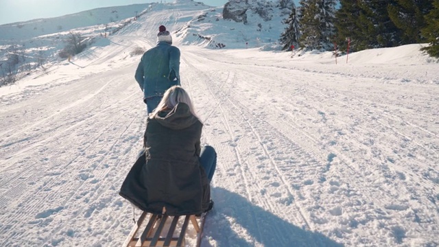 一名年轻男子用雪橇拉着一名年轻女子爬上雪山视频素材