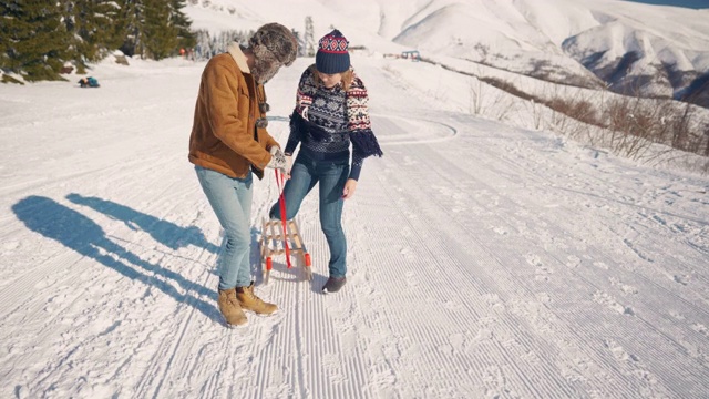 在一个阳光明媚的雪天，男朋友拉着他女朋友的雪橇上山视频素材