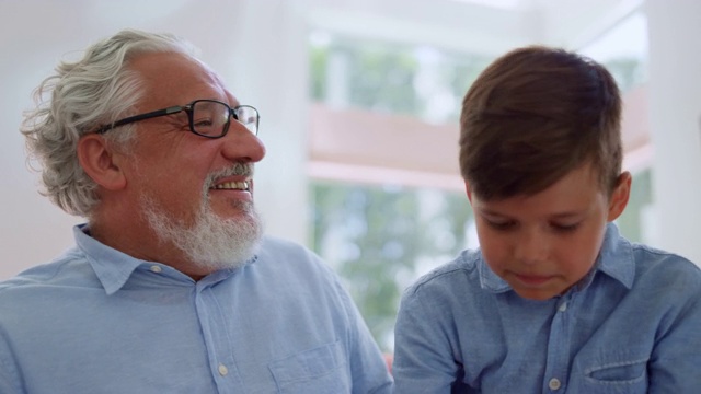 微笑的爷爷看着孙子。快乐的男孩坐在祖父母的腿上视频素材
