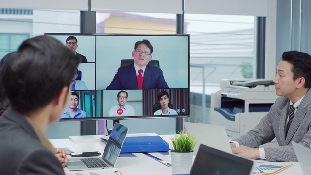 一群商务人士在董事会会议室与一位同事进行视频通话。视频素材