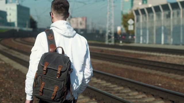 年轻的白人男子与背包沿着铁路轨道调整背包。视频下载