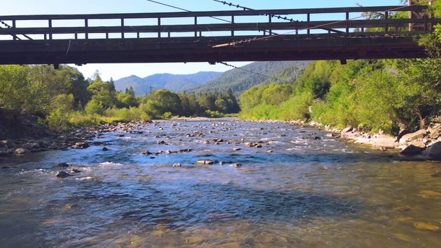 在河上的木桥下飞行。无人机从桥下飞过，低低地飞过河流和岩石。视频下载