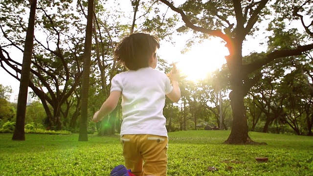 一个穿着白色衬衫的男孩在花园里奔跑，手里拿着一架木制飞机，一个儿童玩具，在太阳即将升起的时候向前奔跑，传递着孩子们的想象力。谁都想追随梦想。视频素材