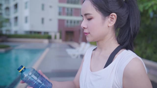 亚洲年轻女性在健身中心锻炼后喝塑料瓶里的水提神饮料放松锻炼后，休息一下，保持水分健康健康活力，感觉新鲜视频素材