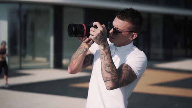 纹身的男摄影师戴着太阳镜，拿着相机拍照视频素材