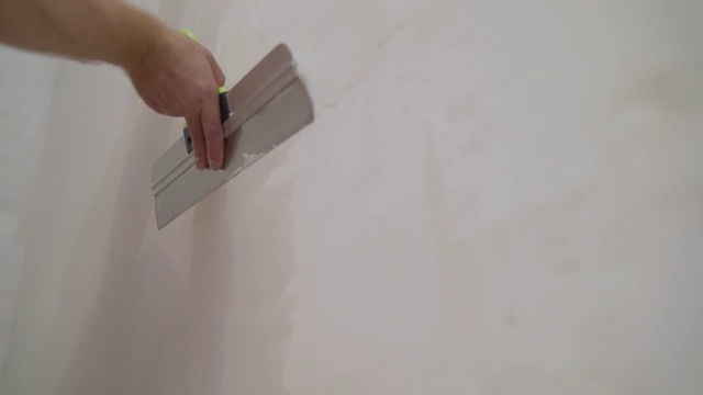 建筑工人用长抹刀抹墙。工人用抹刀和油灰把墙壁对准视频素材