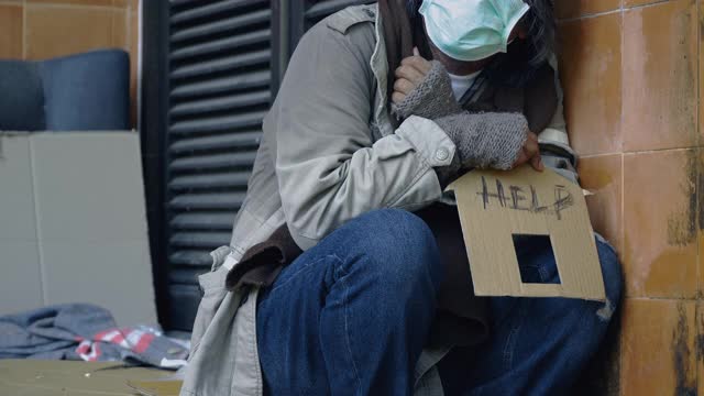 一个无家可归的人坐在砖墙附近的街道上寻求帮助。视频素材