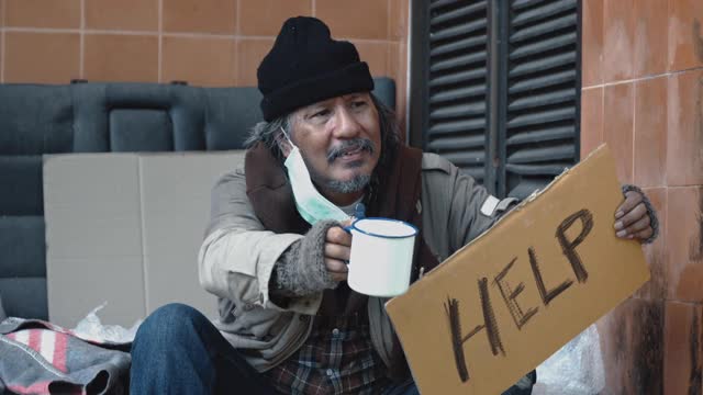 无家可归的乞丐手拿着钱在大街上乞求帮助。视频素材
